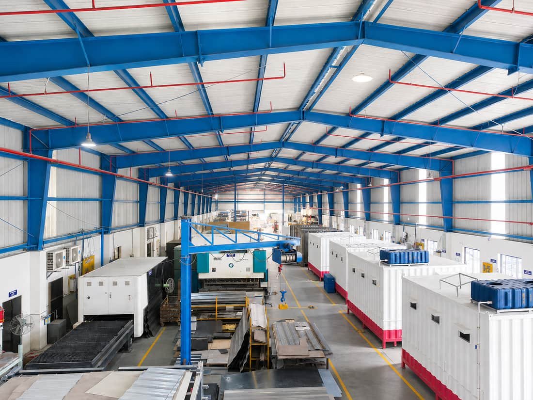 The Finex Industries shop floor: blue portal frames, sheet-metal machinery and completed shelter units